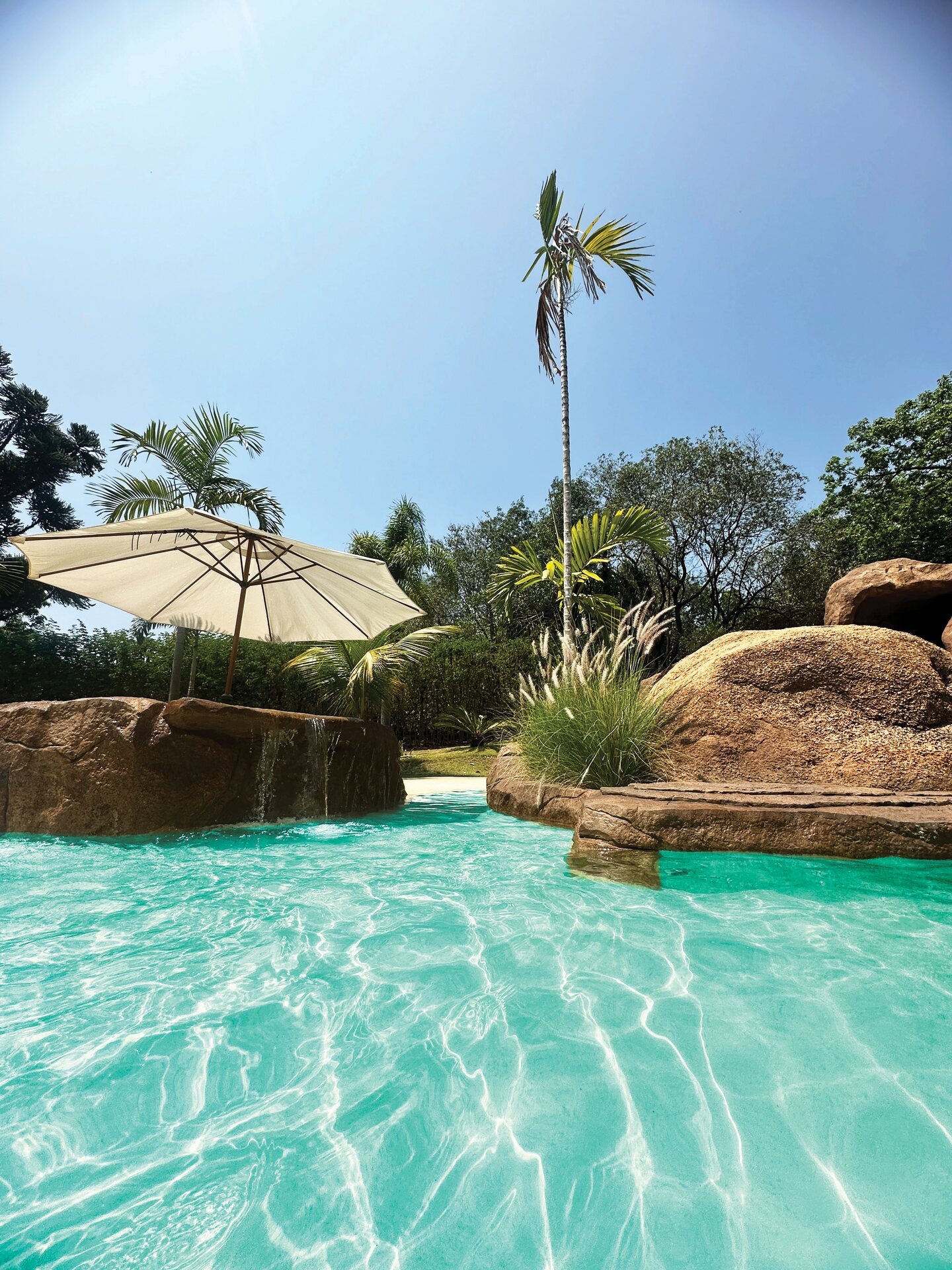 Piscina com água em cores exuberantes, com ombrelone e rochas