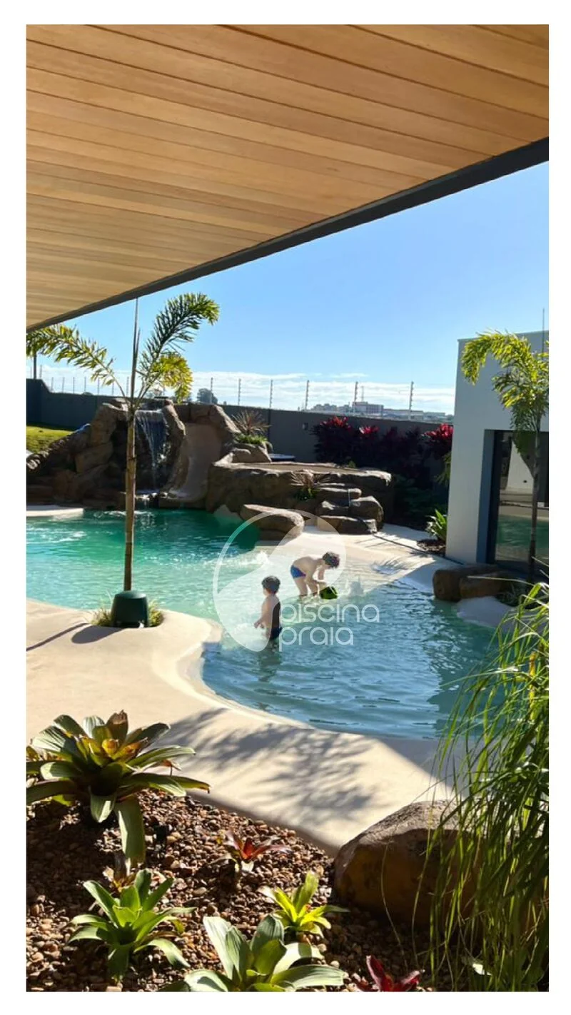 Piscina com rocha e cascata sob cobertura de madeira, criança brincando na água