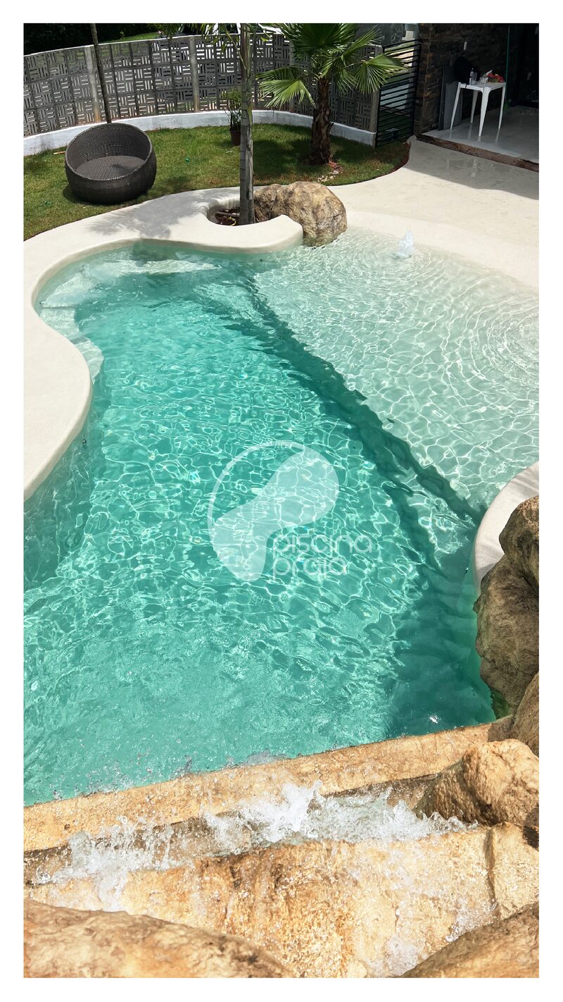 Piscina de borda orgânica com rochas, jardim tropical e balanço suspenso