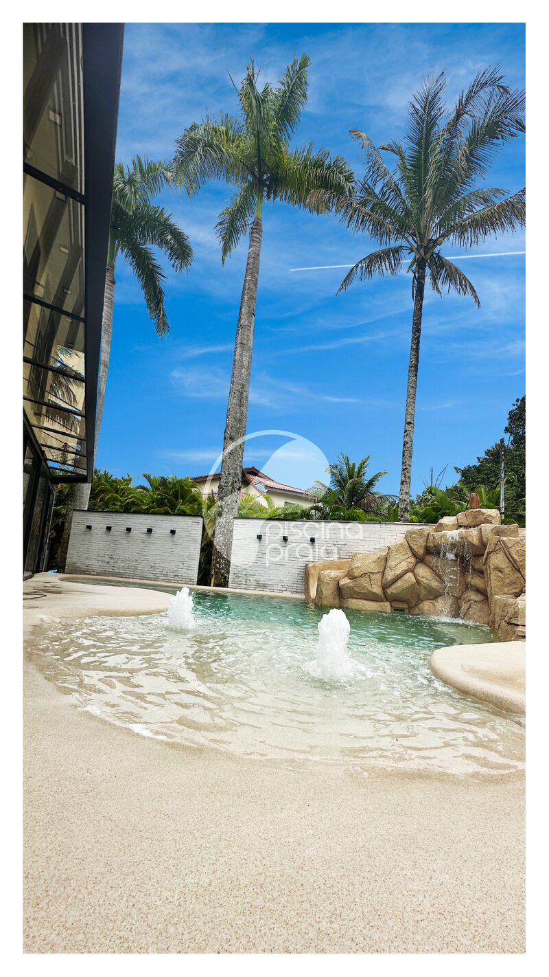 Piscina com jatos de água, prainha de areia e coqueiros altos