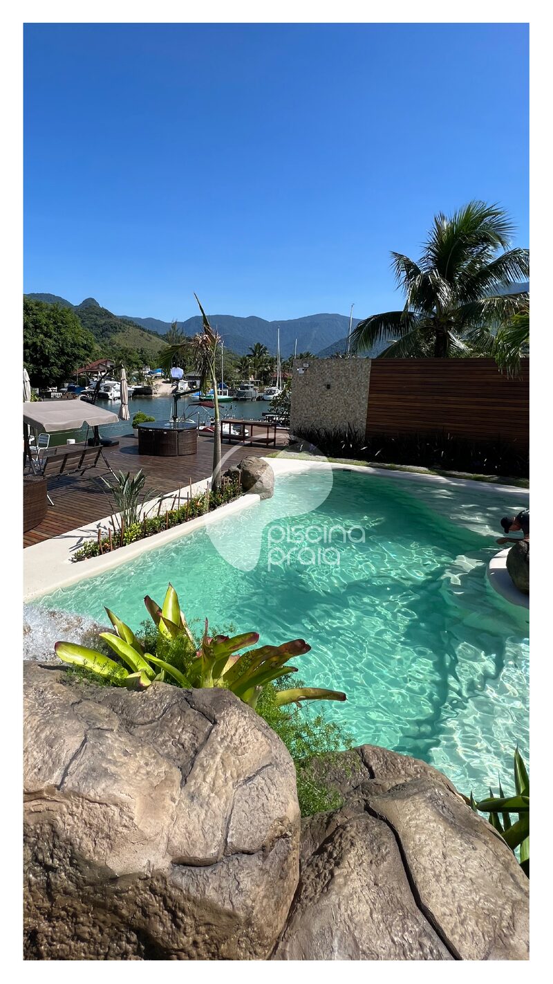 Piscina com rochas e deck de madeira, com montanhas ao fundo