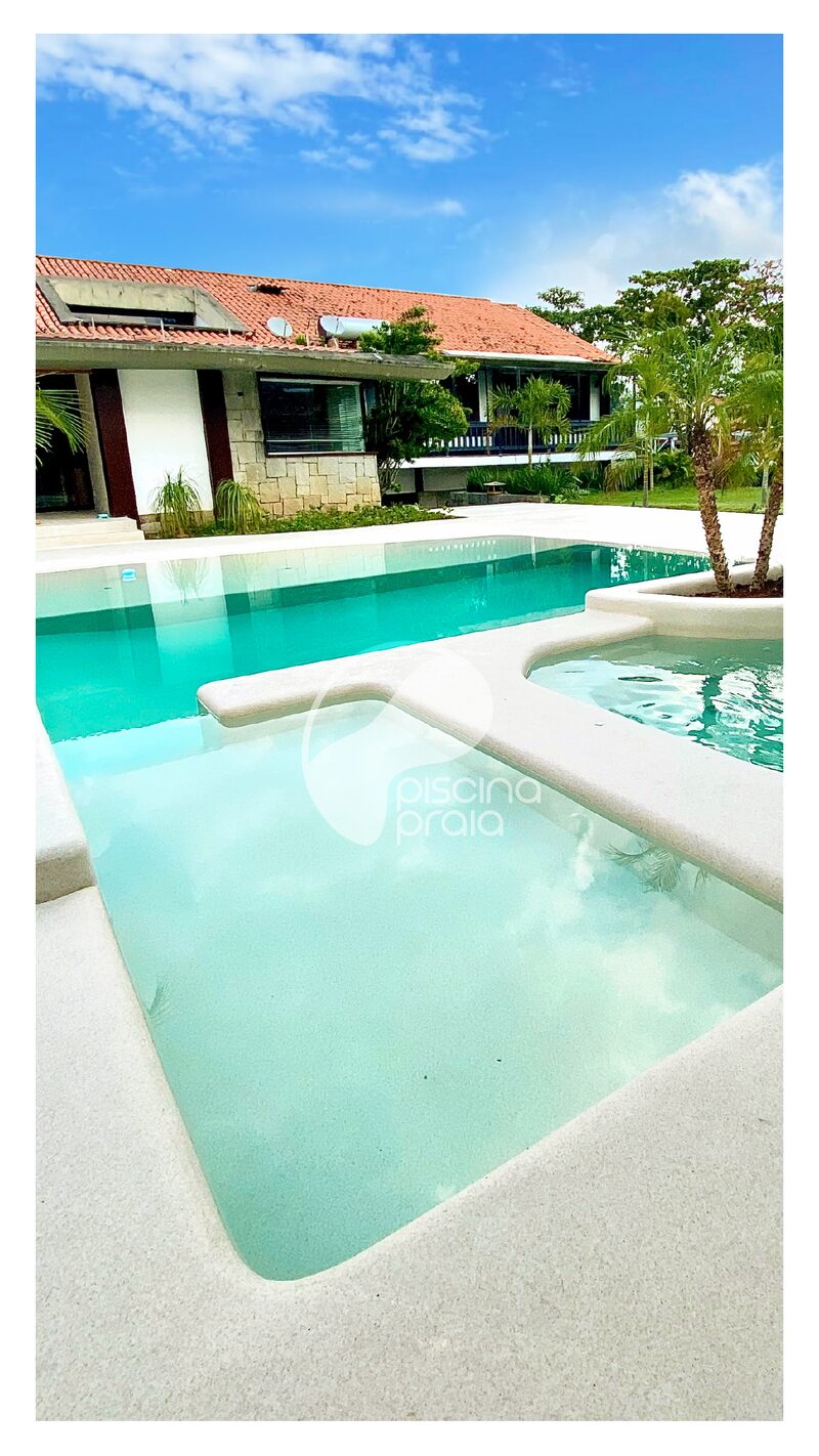 Piscina residencial com prainha de acesso e a casa ao fundo