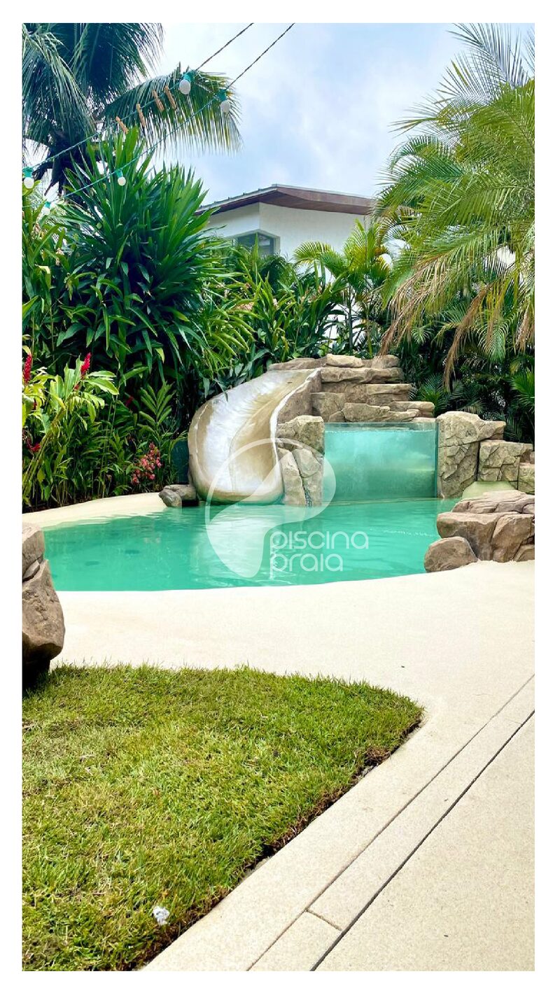 Piscina com escorregador de rocha, gramado e jardim tropical