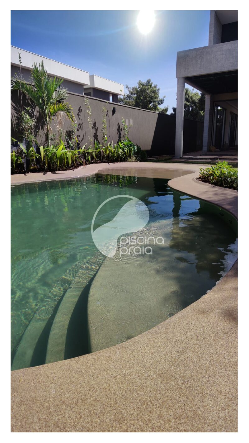 Piscina de fundo escuro com prainha de areia junto à casa de concreto