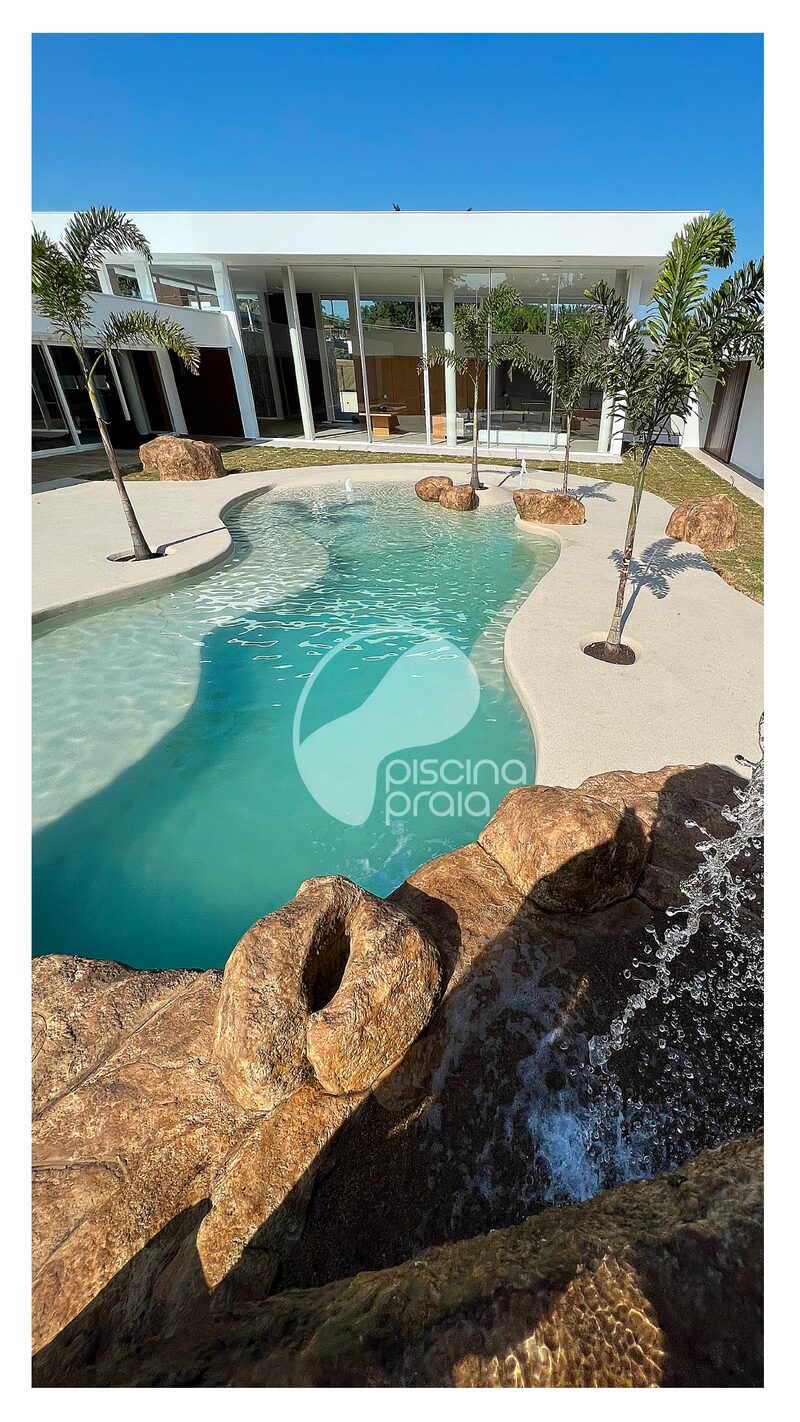 Piscina com cascata de rochas em frente à casa de vidro