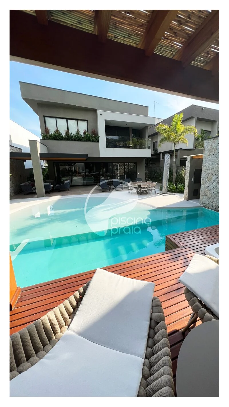 Piscina com deck de madeira e espreguiçadeiras junto à casa moderna